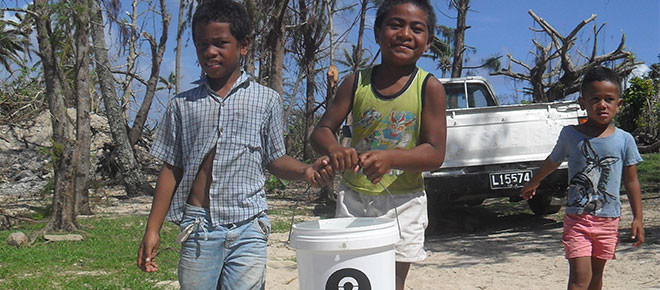 Kids carrying a bucket of water provided by Oxfam in Tonga after Cyclone Ian
