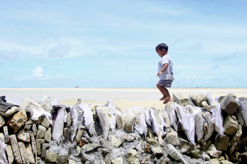 Child walks over a makeshift seawall built in Kiribati